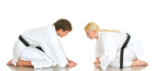 Young karate talented charming girl and young guy sit on their knees in a kimono suit with eyes closed on a white background. Concept preparation for battle. Advertising space