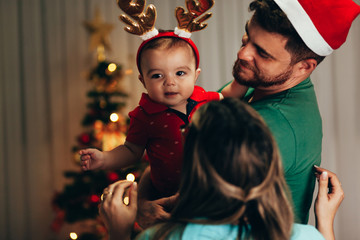 Wall Mural - Young family celebrating Christmas at home. Happy young family enjoying their holiday time together.