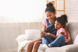 © Prostock-studio - Cheerful african sisters using cellphone at home