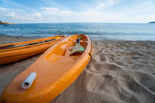 Two Colorful Orange Kayaks On A Sandy Beach Ready For Paddlers In Sunny Day. Several Orange Recreational Boats On The Sand. Active Tourism And Water Recreation.