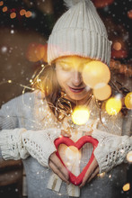   Portrait Of A Young Woman With Many Christmas Lights And A Heart In Her Hand As A Present