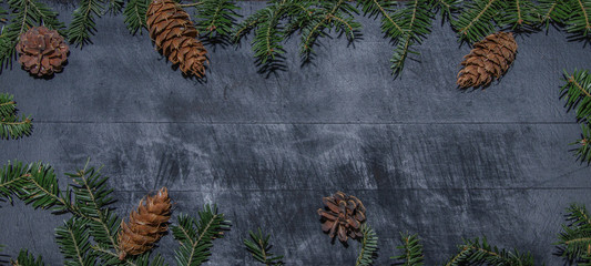 Frame of natural fir pine branches and cones on rustic dark black grey wooden table - christmas background panorama banner long - top view