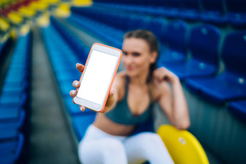 Wall Mural - Sporty woman showing white mobile screen in grandstand