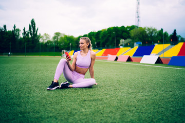 Wall Mural - Thoughtful adult fit female browsing smartphone on sports ground