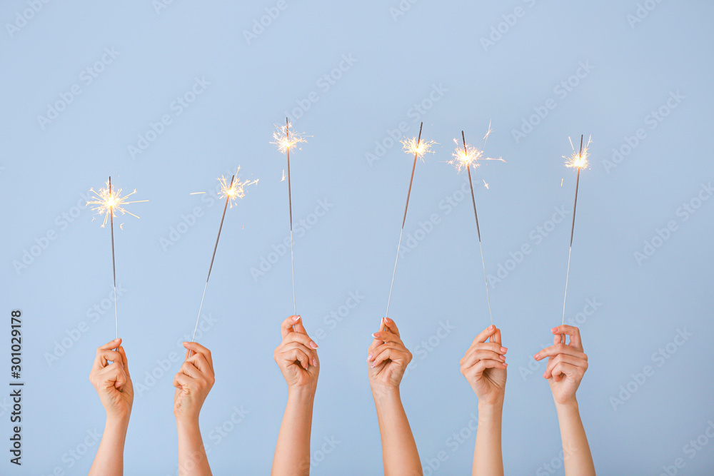 Female hands with Christmas sparklers on color background
