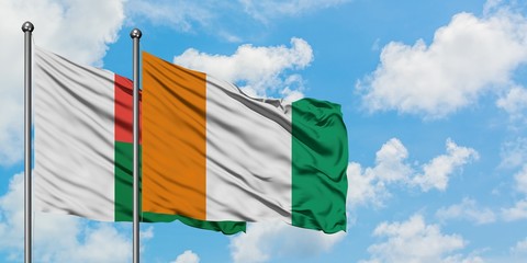 Madagascar and Cote D'Ivoire flag waving in the wind against white cloudy blue sky together. Diplomacy concept, international relations.