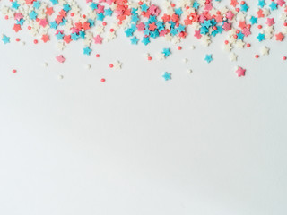 Festive border frame of colorful pastel sprinkles on white background, copy space bottom. Sugar sprinkle dots and stars, decoration for cake and bakery. Top view or flat lay