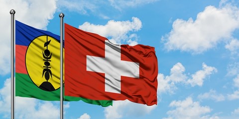 Poster - New Caledonia and Switzerland flag waving in the wind against white cloudy blue sky together. Diplomacy concept, international relations.