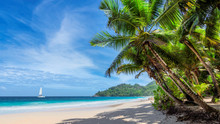 Tropical White Sand Beach With Coconut Palm Trees And A Sailing Boat In Turquoise Sea On Seychelles Tropical Island.