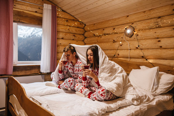 Teen friends in same Christmas pajamas relaxing in bed inside cozy log cabin with winter view