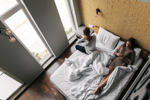 Young Girl And Guy Relaxing On Comfy Bed In Modern Hotel Room