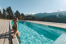 Young Woman Spending Vacation In Swimming Pool With Mountain Landscape
