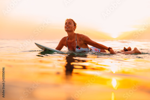 Fototapeta na szkło Atrakcyjna surfingowiec kobieta na surfboard w oceanie. Surfgirl o zachodzie słońca