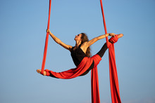 Beautiful And Flexible Female Circus Artist Dancing With Aerial Silk On A Sky Background