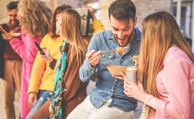 Happy friends eating street food outdoor - Young trendy people having fun together drinking and laughing around downtown streets - City lifestyle and party concept - Focus on right man face