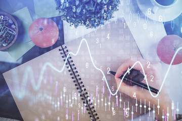 Forex chart hologram on hand taking notes background. Concept of analysis. Double exposure