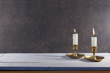 Burning two candles in vintage metal candlestick on white wooden table and copy space on dark stone background..