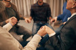 © AnnaStills - Close-up of people sitting on chairs in circle and holding hands they visiting therapy lesson