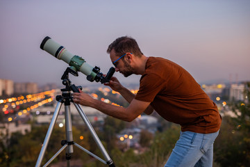 Wall Mural - astronomer with a telescope watching at the stars and moon with blurred city lights in the backgroun