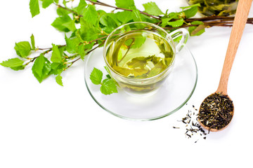 Wall Mural - Glass cup of green tea with green natural birch branches and dry tea in a wooden spoon isolated on a white background. 