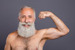 © deagreez - I'm superman. Photo of aged retired handsome man neat long beard showing strong naked shirtless shoulders raise fists strong biceps looking mirror isolated grey background