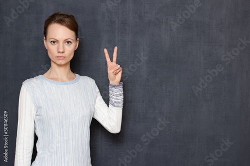 Fotografía Portrait of serious focused young woman showing peace gesture