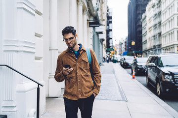 Frowning ethnic young man using smartphone on street