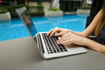Wall Mural - close up woman hands pressing keyboard on laptop sunny day swimm