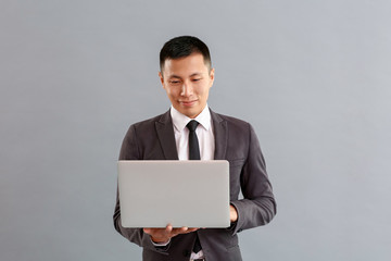 Asian businessman with laptop on grey background