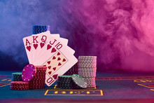 Winning Combination In Poker Leaning On Colored Chips Piles On Blue Cover Of Playing Table. Black, Smoke Background, Red And Blue Backlights. Casino.