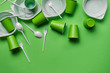 White plastic disposable tableware on green background with copy space. The concept of picnic utensil. Top view. Selective focus. Close-up.