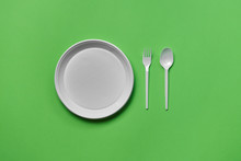 White Plastic Disposable Tableware On Green Background With Copy Space. The Concept Of Picnic Utensil. Top View. Selective Focus. Close-up.