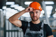 © standret - Touching protective helmet. Industrial worker indoors in factory. Young technician with orange hard hat