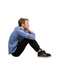 Full Length Side View Of Upset And Tired Boy Teenager Sitting On The Floor Keeps Hand Under Chin Looking Ahead Thoughtful Isolated Over White Background With Copy Space.