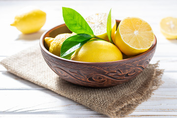 Fresh organic juicy lemons in a clay bowl on white kitchen table. Healthy and organic food concept.