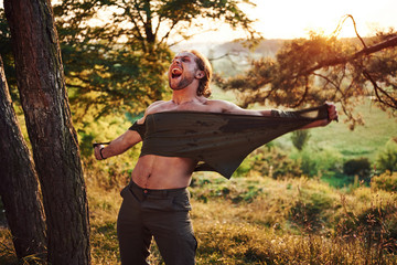 Screaming and tearing the shirt. Conception of freedom. Beautiful man in the forest. Good weather. Beautiful orange colored sunlight