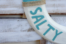 This Found Typography Is Carved Onto A White And Teal Wooden Life Ring Or Life Saver Which Contains The Word SALTY.  The Addition Of Twine Completes Its Nautical Look.