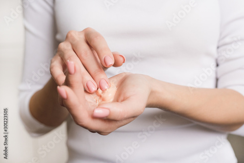 Cuadros en Lienzo Beautiful young girl in white longsleeve moisturizes her hands with cream