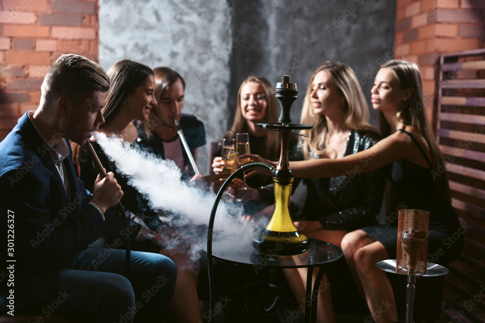 Shisha Community Friends party in hookah lounge. Group of people women and men smoking ...