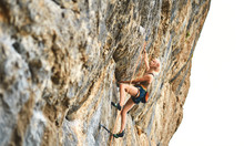 Side View Of Young Athletic Woman Rock Climber Climbing On The Cliff. A Woman Climbs On A Vertical Rock Wall On White Background. Conquering, Overcoming And Active Lifestyle Concept.
