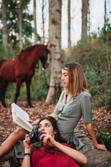 Wall Mural - Young women reading a book and taking photos in the forest