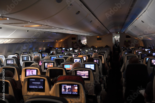 Interior of a jet airplane on a long international flight with TV screens on the back of seats