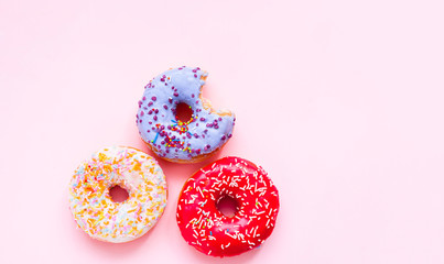 Wall Mural - Bitten colored donuts with colorful sprinkles on pink background. Close-up