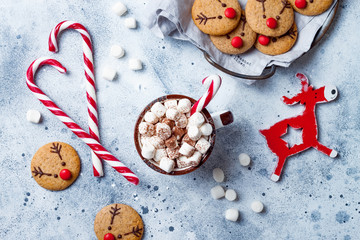 Wall Mural - Hot cocoa with marshmallow in ceramic mug surrounded by Christmas gingerbread. Decorated red nosed reindeer cookies. Festive homemade decorated sweets