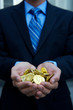 Unrecognizable businessman holding a handful of gold treasure coins standing outdoors in a dark suit