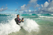 © PeskyMonkey - Overwhelmed young businessman in a full suit having a rough time using his tablet computer to surf the web in crashing waves on the shore of a tropical beach