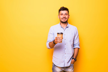 Portrait of man taking coffee in takeaway paper cup over isolated yellow studio background