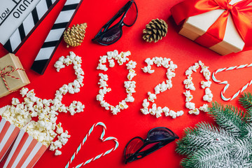 Clapperboard, popcorn, 3d glasses, cande cane, christmas gifts in a red paper background. Flat lay. Top view. Christmas concept