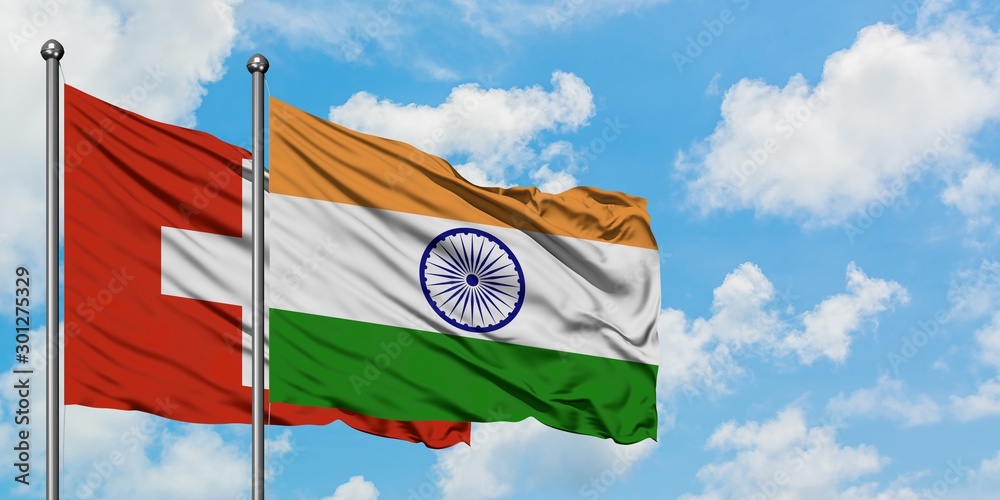 Switzerland and India flag waving in the wind against white cloudy blue ...