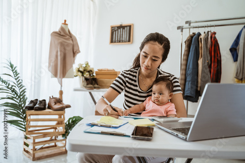 Fotomural portrait of woman with baby working from home of her online ecommerce shop